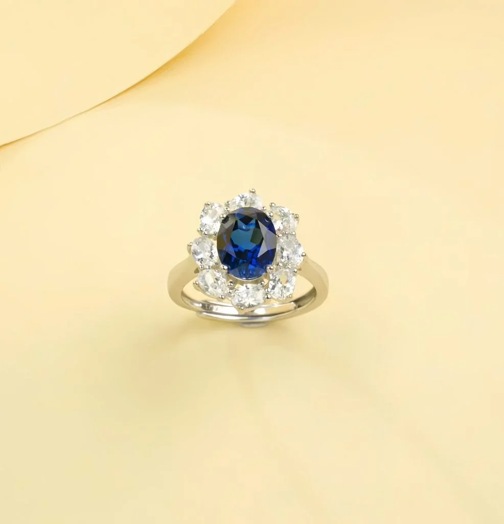 Elegant lifestyle product photo of lab-grown blue sapphire sunflower halo ring with diamond halo, displayed on warm yellow background