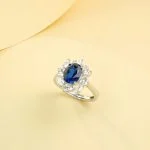 Lab-grown blue sapphire sunflower halo ring with lab-created diamond halo, displayed on warm yellow background, elegant product photography