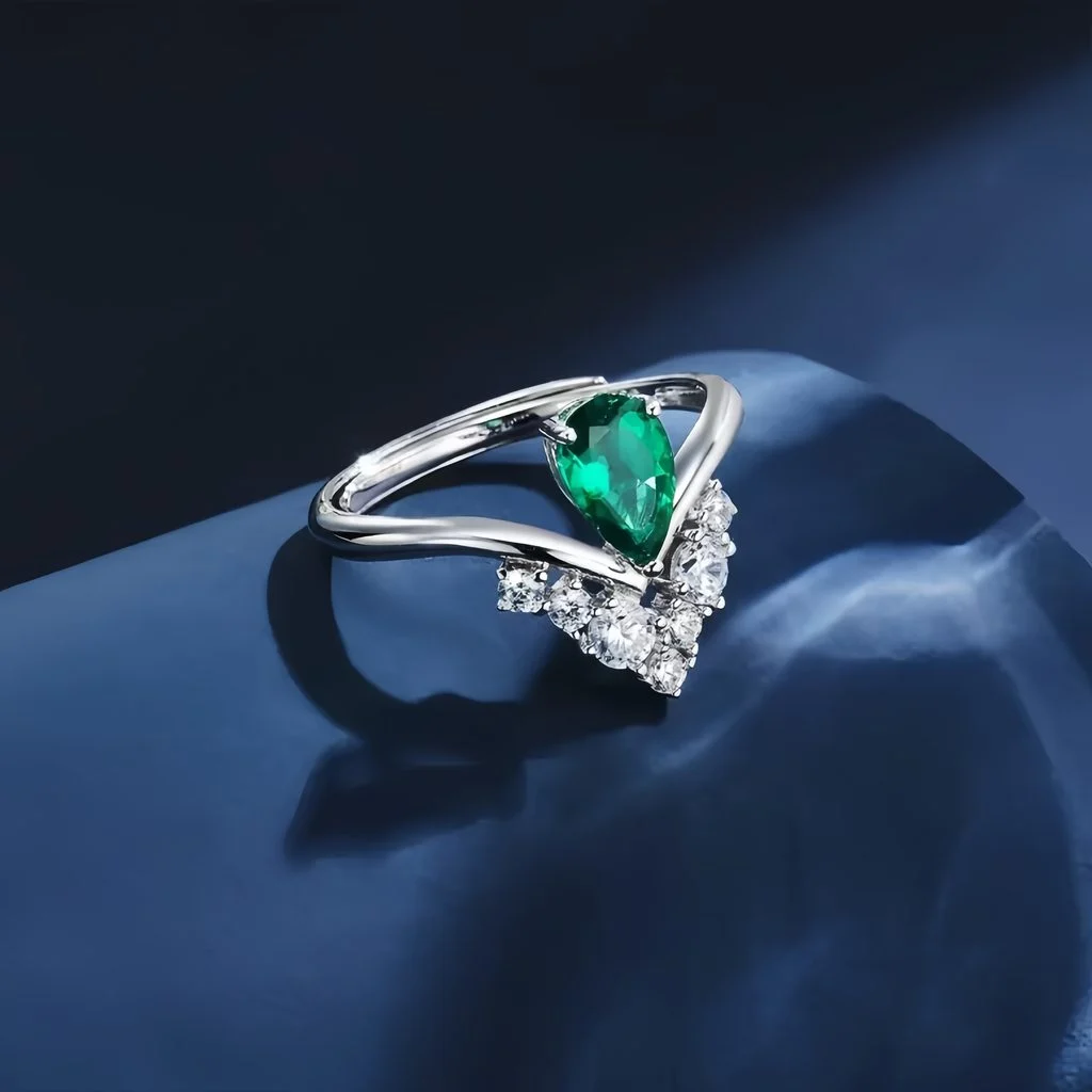 Lab-grown emerald crown ring with V-shaped diamond setting resting on deep blue silk fabric, luxury jewelry photography