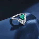 Lab-grown emerald pear-cut ring with V-shaped crown setting resting on deep blue silk fabric, luxury jewelry photography