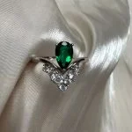 Lab-grown emerald pear-cut ring with V-shaped crown setting resting on white silk fabric, soft romantic jewelry photography for weddings and engagements