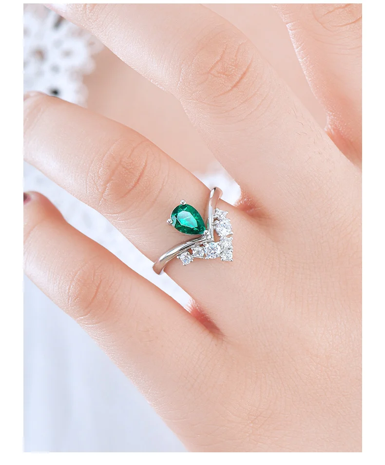 Close-up of hand wearing lab-grown emerald crown ring showing V-shaped diamond band, natural light on lace background