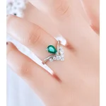 Close-up of hand wearing lab-grown emerald crown ring showing V-shaped band design and pear-cut emerald on finger, natural light photography