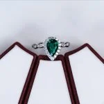 top down flat lay lab grown emerald green pear diamond halo ring on black background S925 silver