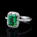 lab grown emerald halo ring S925 sterling silver on black reflective background emerald cut green gemstone baguette round diamond halo pavé band