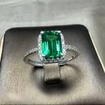 lab grown emerald halo ring S925 sterling silver on gray display surface emerald cut green gemstone baguette round diamond halo pavé band