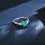 lab grown emerald three stone ring S925 sterling silver on dark background emerald cut green gemstone pear shaped diamond accents adjustable open band
