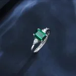 lab grown emerald three stone ring S925 sterling silver angle view on dark background emerald cut green gemstone pear shaped diamond accents adjustable band