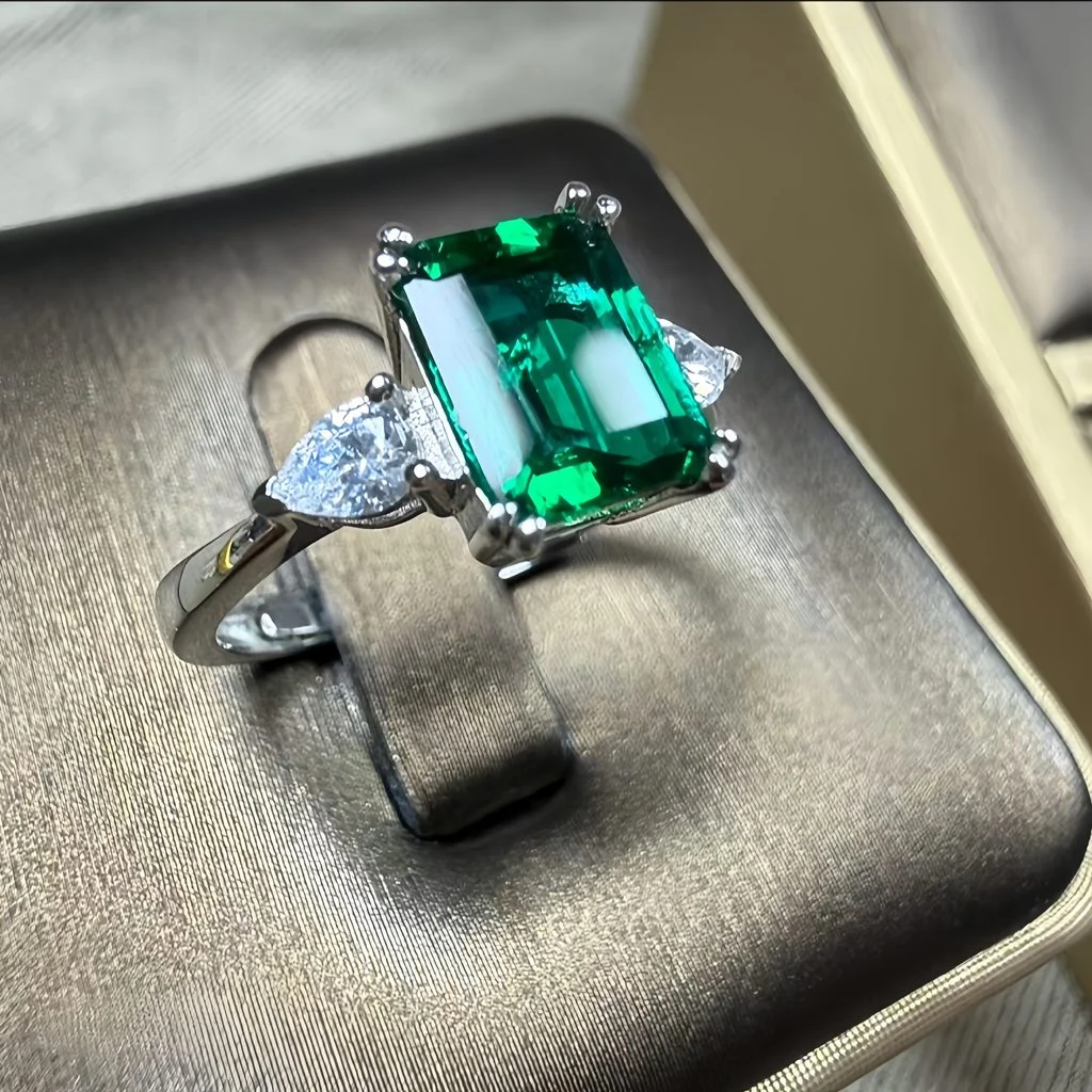  lab grown emerald three stone ring S925 sterling silver detail close-up emerald cut green gemstone pear shaped diamond accents prong setting step cut facets