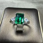 lab grown emerald three stone ring S925 sterling silver detail close-up emerald cut green gemstone pear shaped diamond accents prong setting