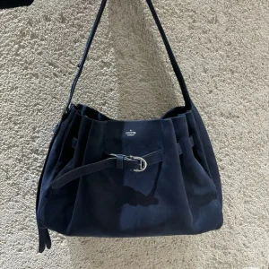 Navy genuine leather buckle hobo shoulder tote bag, front view against textured wall