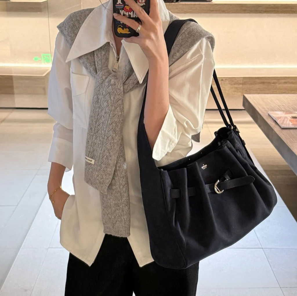 Woman wearing navy slouchy genuine leather hobo bag over shoulder with white shirt, casual office everyday outfit