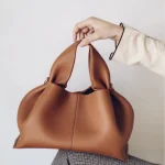 Dark brown vintage suede cloud bag worn on shoulder, retro dumpling handbag with push-lock clasp