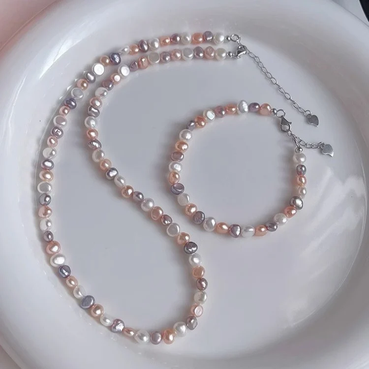 Natural freshwater baroque pearl necklace and bracelet set on white ceramic plate, featuring multicolor pearls in white, peach, lavender, and rose gold tones with silver-toned lobster clasp and heart-shaped extender charm by MAISON ELARA & CO