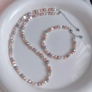 Natural freshwater baroque pearl necklace and bracelet set on white ceramic plate, featuring multicolor pearls in white, peach, lavender, and rose gold tones with silver-toned lobster clasp and heart-shaped extender charm by MAISON ELARA & CO