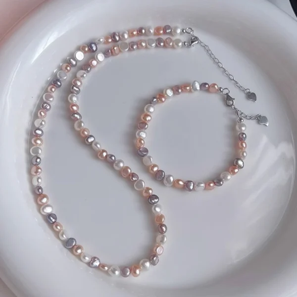 Natural freshwater baroque pearl necklace and bracelet set on white ceramic plate, featuring multicolor pearls in white, peach, lavender, and rose gold tones with silver-toned lobster clasp and heart-shaped extender charm by MAISON ELARA & CO