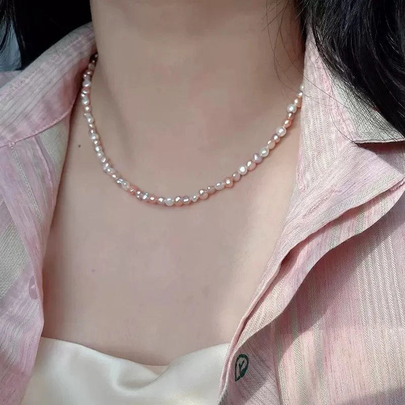 Close-up of model wrist wearing natural freshwater baroque pearl bracelet, showing multicolor pearls in white, peach, lavender, and rose gold tones with silver-toned lobster clasp and heart-shaped extender charm against white clothing background by MAISON ELARA & CO