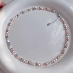 Natural freshwater baroque pearl necklace arranged in circular shape on white background, showing multicolor pearls in peach, lavender, white, and rose gold tones with silver-toned clasp and heart-shaped extender charm by MAISON ELARA & CO