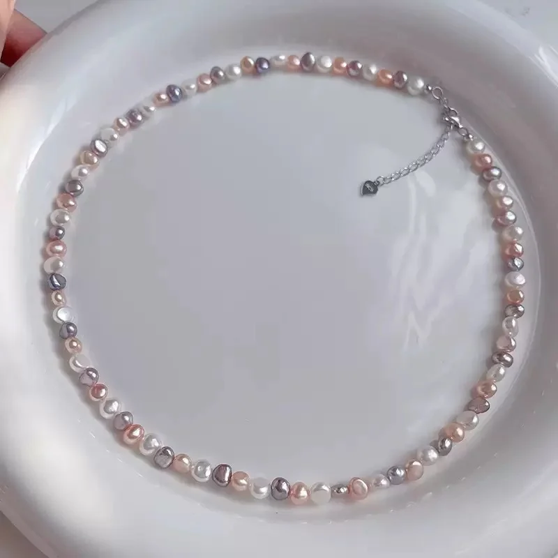 Natural freshwater baroque pearl necklace arranged in circular shape on white background, showing multicolor pearls in white, peach, lavender, and rose gold tones with silver-toned lobster clasp and heart-shaped extender charm by MAISON ELARA & CO