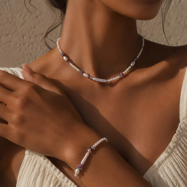 Model wearing dopamine freshwater pearl and colorful crystal beaded necklace and bracelet set, showing small round pearls, baroque pearl pendants, and cobalt blue ruby red soft pink crystal beads with gold-toned clasp, paired with cream ribbed top by MAISON ELARA & CO