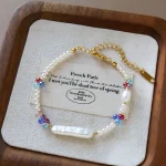 Close-up of dopamine freshwater pearl and colorful crystal beaded bracelet on white display card, showing small round pearls, baroque pearl pendant, cobalt blue ruby red and soft pink crystal beads, and gold-toned clasp with extension chain on wooden surface by MAISON ELARA & CO