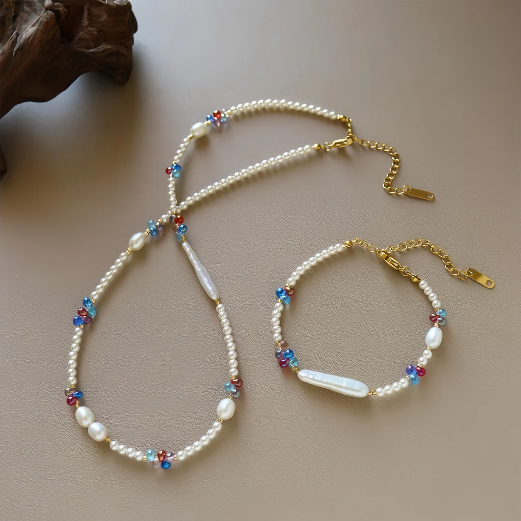 Close-up of dopamine freshwater pearl and colorful crystal beaded bracelet on white display card in wooden tray, showing small round pearls, baroque and biwa freshwater pearls, cobalt blue ruby red and soft pink crystal bead clusters, and gold-toned clasp with extension chain by MAISON ELARA & CO