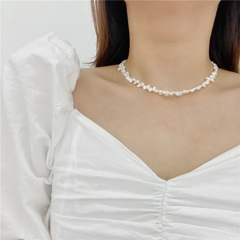 Model wearing French baroque natural freshwater pearl choker necklace with white ruffled sweetheart neckline top, showing irregular organic shaped pearls in ivory white cream tones at collarbone length with gold-toned clasp close-up by MAISON ELARA & CO