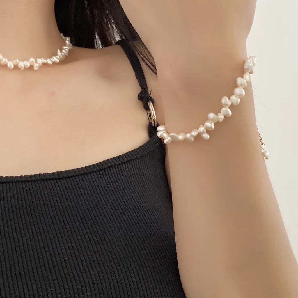 Model wearing French baroque natural freshwater pearl necklace and bracelet with hands near neck, showing irregular organic shaped pearls in ivory white cream tones with gold-toned clasp and extender chain lifestyle portrait by MAISON ELARA & CO