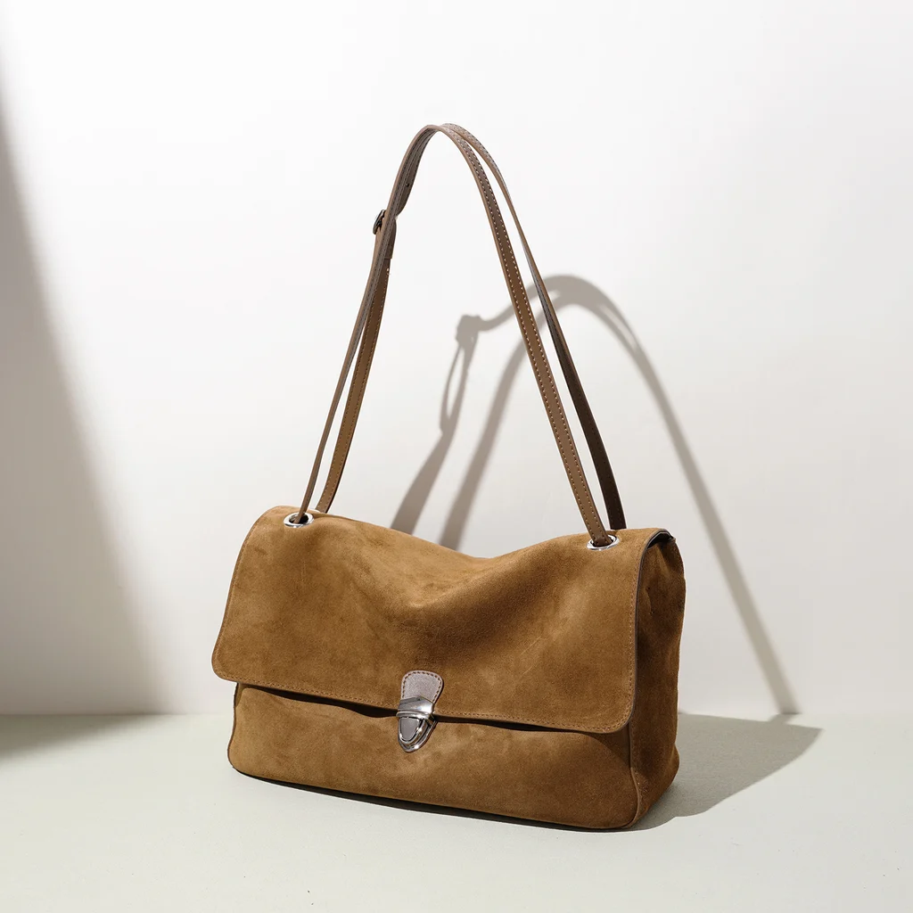 Coffee brown genuine leather shoulder bag shown at three-quarter angle, displaying soft suede-like texture, vintage silver push-lock clasp and slender leather straps with silver metal ring hardware on minimalist white background