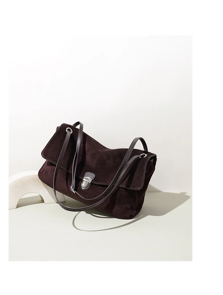 Coffee brown genuine leather shoulder bag displayed on a white sculptural podium, showing soft unstructured silhouette with vintage silver push-lock clasp and slender leather straps against minimalist studio background