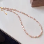 Natural freshwater baroque pearl necklace laid flat on light surface, showing multicolor pearls in white, peach, lavender, and rose gold tones with silver-toned clasp, heart-shaped extender charm, and gift box packaging by MAISON ELARA & CO