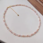 Natural freshwater baroque pearl necklace on light background, showing multicolor pearls in peach, lavender, white, and rose gold tones with silver-toned clasp and heart-shaped extender charm, product flat lay display by MAISON ELARA & CO
