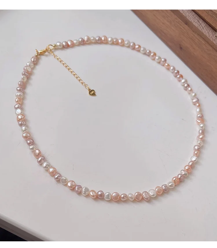 Natural freshwater baroque pearl necklace and bracelet set on white background, showing multicolor pearls in white, peach, lavender, and rose gold tones with silver-toned lobster clasp and heart-shaped extender charm by MAISON ELARA & CO
