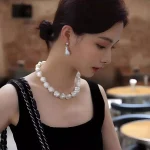 Woman wearing baroque pearl necklace and pearl earrings, side profile elegant styling in warm restaurant setting