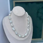 Baroque pearl necklace on white jewelry bust, silver tone irregular freshwater pearls on dark green background