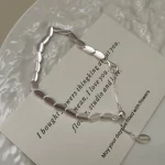S925 sterling silver brushed bean necklace flat lay on light paper background with brand tag, minimalist jewelry