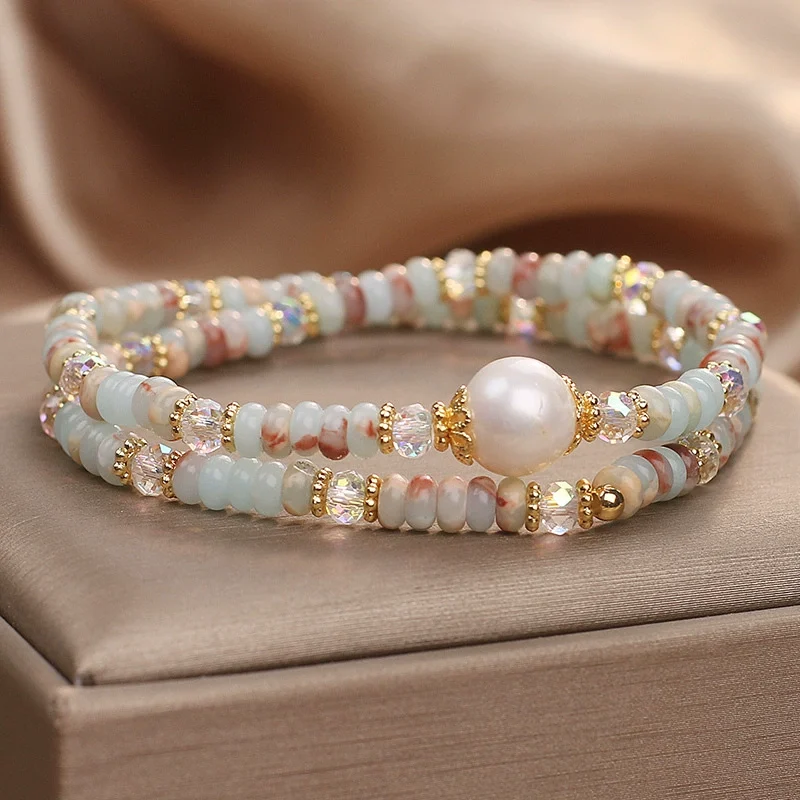 Side angle view of Shoushan stone pearl double-layer bracelet showing dual-strand depth with freshwater pearl focal and faceted AB crystal beads in sky blue milky white and rose tones on beige satin fabric
