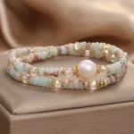 Natural Shoushan stone pearl double-layer bracelet shown on beige satin background, dual-strand design with freshwater pearl focal stone and faceted AB crystal beads in sky blue milky white and rose tones