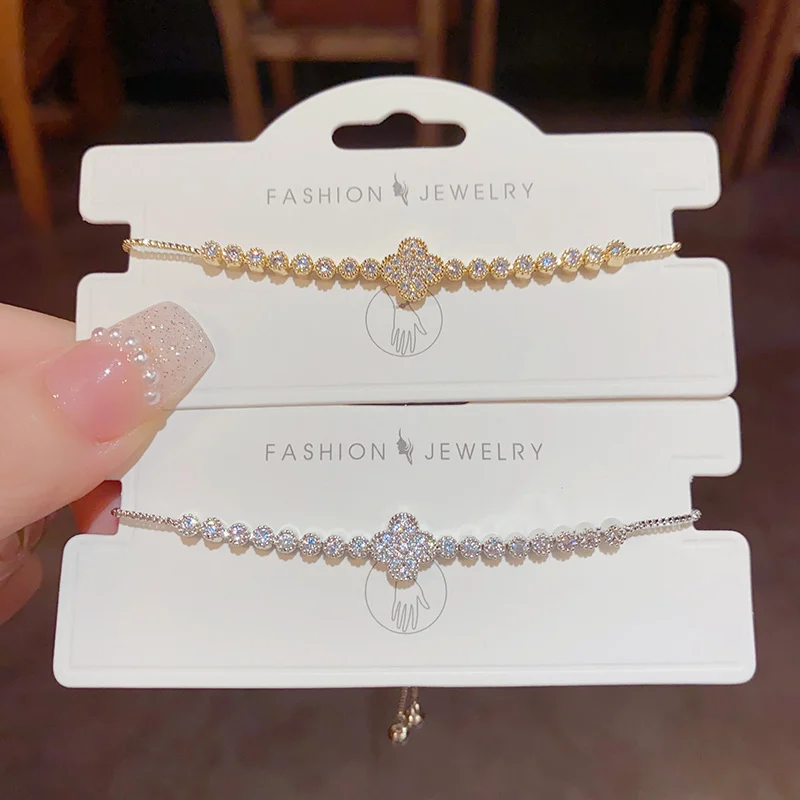 Elegant zircon four-leaf clover bracelet in gold-tone and silver-tone finishes displayed on white jewelry cards, showing sparkling micro-pavé tennis bracelet design with adjustable sliding clasp closure