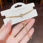Gold-tone zircon four-leaf clover bracelet displayed on white jewelry card, showing sparkling champagne zircon stones in micro-pave tennis bracelet setting with warm golden metal finish