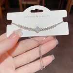 Silver-tone zircon four-leaf clover bracelet displayed on white jewelry card, showing sparkling clear white zircon stones in micro-pave tennis bracelet setting with cool silver metal finish