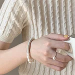 Natural baroque freshwater pearl bracelet worn on wrist with cream cable-knit sweater sleeve, showing 999 fine silver curved tube accent and irregular organic pearl shapes in lifestyle styling context