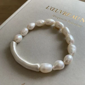 Natural baroque freshwater pearl bracelet with 999 fine silver curved tube accent on book surface, showing irregular organic pearl shapes with milky white cream tones and subtle iridescent overtones