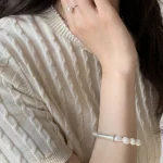 Natural baroque freshwater pearl bracelet worn on wrist with cream ribbed knit sweater, showing 999 fine silver curved tube accent and irregular organic pearl shapes in warm lifestyle styling