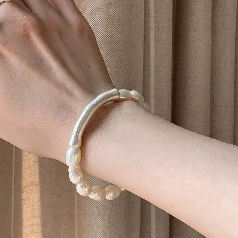Baroque freshwater pearl bracelet worn on wrist showing 999 fine silver curved tube accent and irregular pearl luster against pleated fabric background