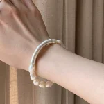 Natural baroque freshwater pearl bracelet worn on wrist showing irregular organic pearl shapes with milky white cream tones and 999 fine silver curved tube accent against warm curtain background