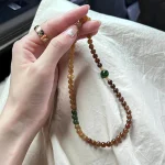Hetian Qiemo sugar jade bracelet held in hand, caramel gradient round jade beads with green jade accent, old money natural stone jewelry for women