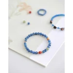 Handmade blue crystal and South Red agate beaded bracelet styled with a matching ring and earrings on a light gray background