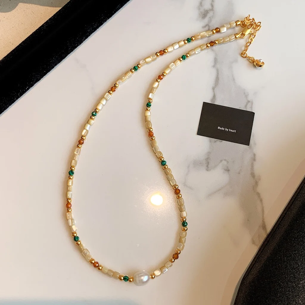 Multi wrap styling of the natural stone and shell beaded necklace with a large baroque pearl, arranged on marble