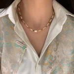Close-up of the natural stone and shell beaded necklace worn over a white shirt and patterned jacket